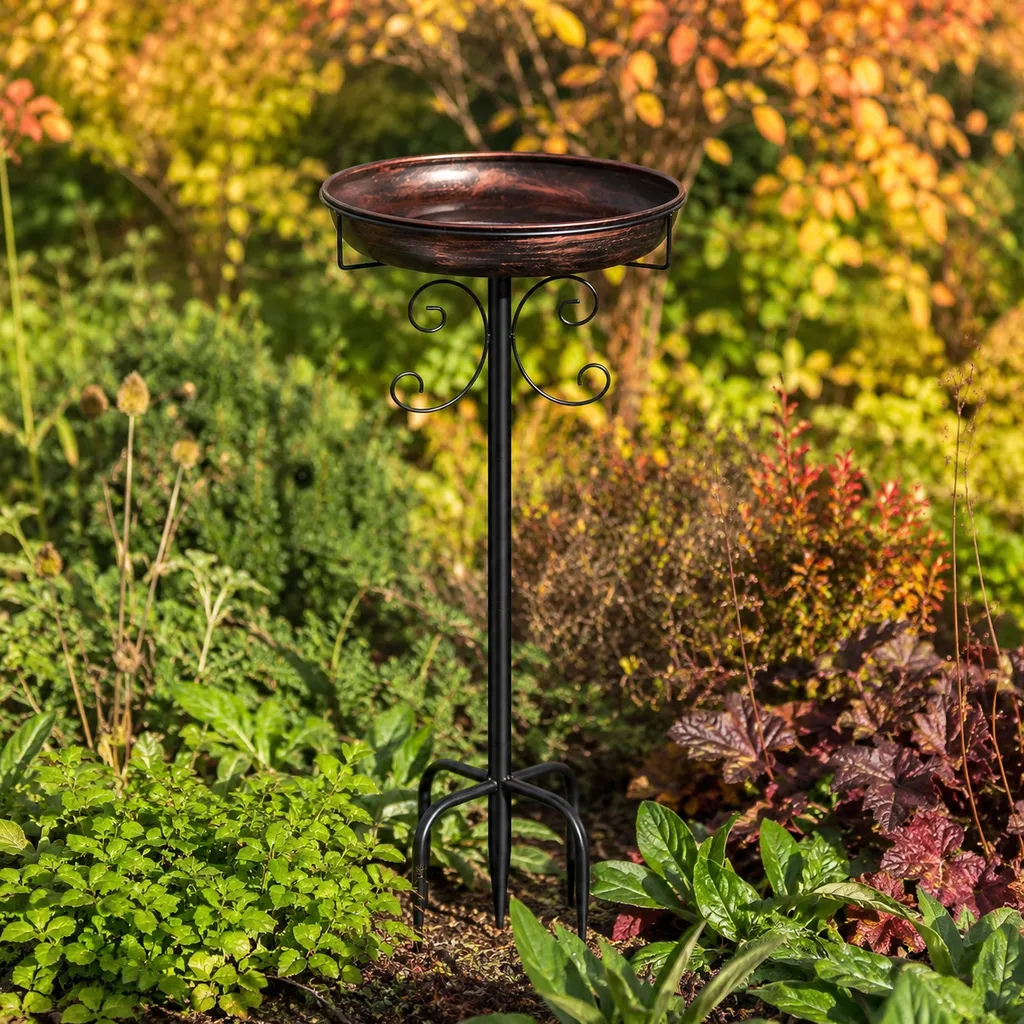 Metal bird bath staked into a garden border among low autumn planting