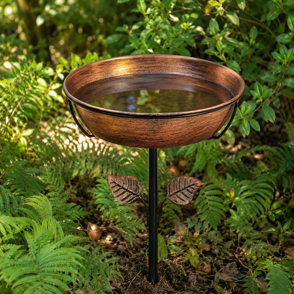 Small staked metal bird bath at ground level among ferns and low shrubs