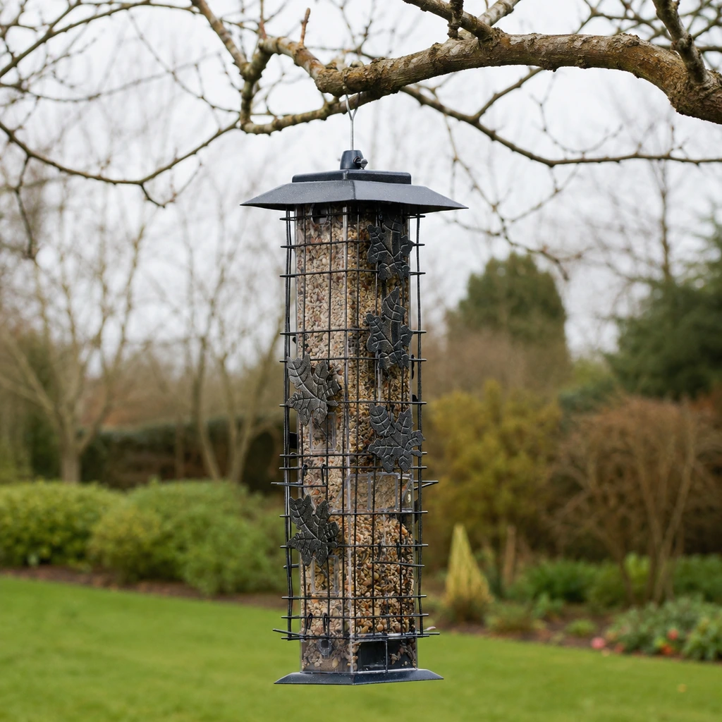 Metal squirrel resistant seed feeder hanging from a bare tree branch by a lawn