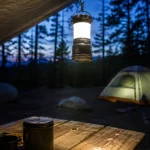 Lit camping lantern hanging over a picnic table at a forest campsite at dusk