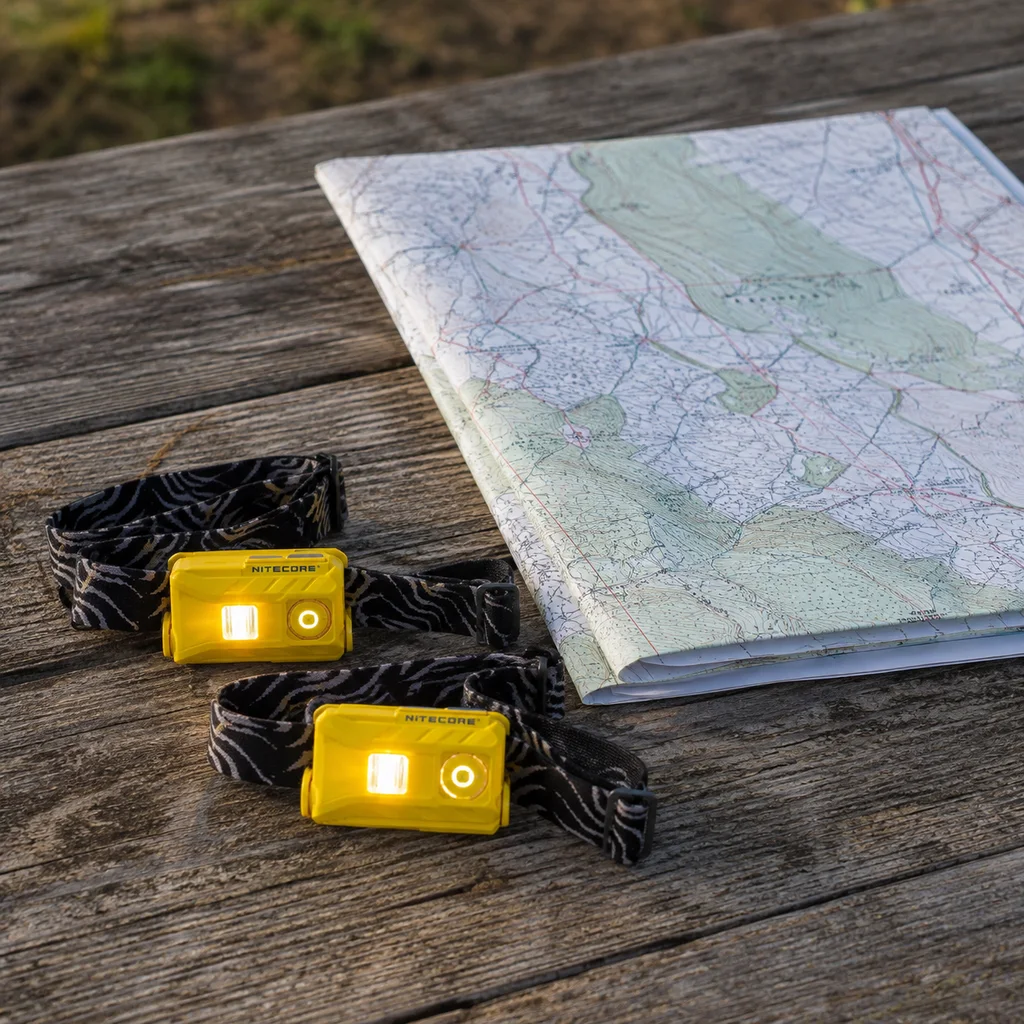 Nitecore NU25 headlamp lit beside a folded paper map showing how small it is