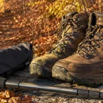 Waterproof mid cut hiking boots on a granite slab beside an autumn leaf covered trail