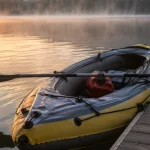Inflatable kayak floating beside a wooden dock on a misty lake at sunrise