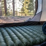 Inflated sleeping pad and rolled sleeping bag inside a tent at a forest campsite