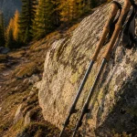 Cork grip trekking poles leaning against a granite boulder on an autumn mountain trail