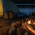 Camping for beginners setup with a lantern, campfire and tent beside a lake at dusk