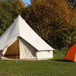 A cream canvas bell tent and an orange nylon dome tent pitched side by side