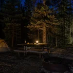 Campsite at dusk showing dim tent light, table light and a bright beam down a path