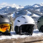 Three ski helmets lined up on a snowy rail at the top of a mountain run