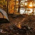 Fall camping essentials at a golden hour campsite with a tent and campfire