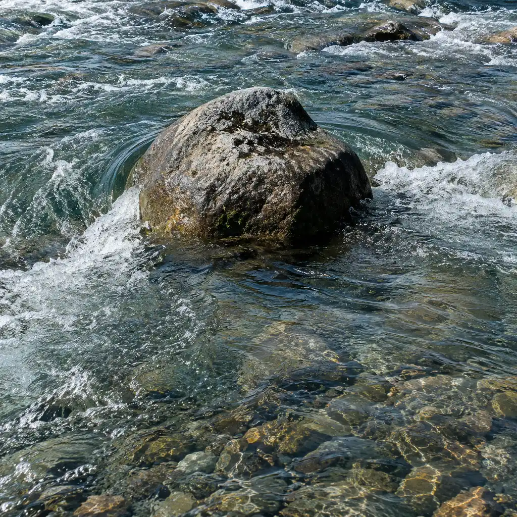 A boulder breaking the surface with a calm holding pocket just downstream