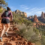 Trail runner climbing a red rock switchback trail in Sedona, Arizona at morning light