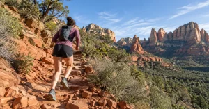 Trail runner climbing a red rock switchback trail in Sedona, Arizona at morning light